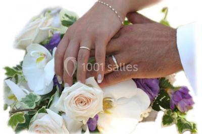 Miniature Location salle Montmorency (Val-d'Oise) - Le Concept Réception #12 Mains d'un couple portant des alliances, posées sur un bouquet de fleurs blanches et violettes.