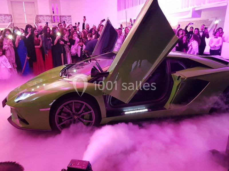 Location salle Saint-Germain-lès-Arpajon (Essonne) - Voilier 91 #8 Voiture de sport verte aux portes papillon ouvertes, entourée de fumée et d'une foule dans un lieu éclairé.