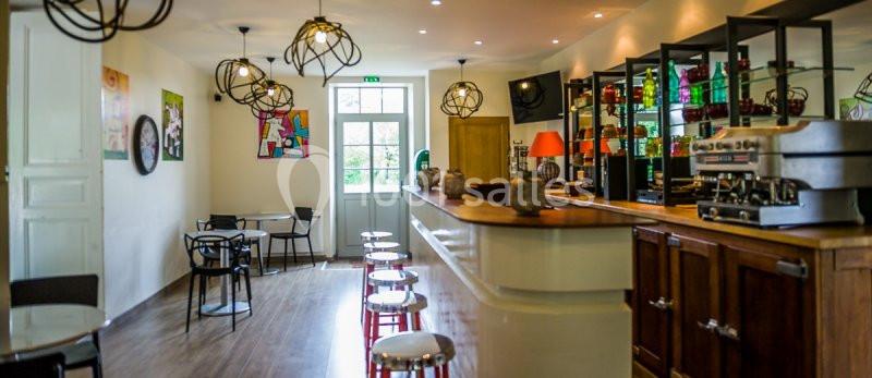 Intérieur d'un café moderne avec comptoir en bois, tabourets, tables, et luminaires suspendus.