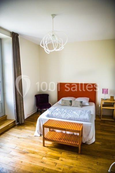 Chambre lumineuse avec lit double, tête de lit orange, parquet en bois, table de chevet et fauteuil violet.