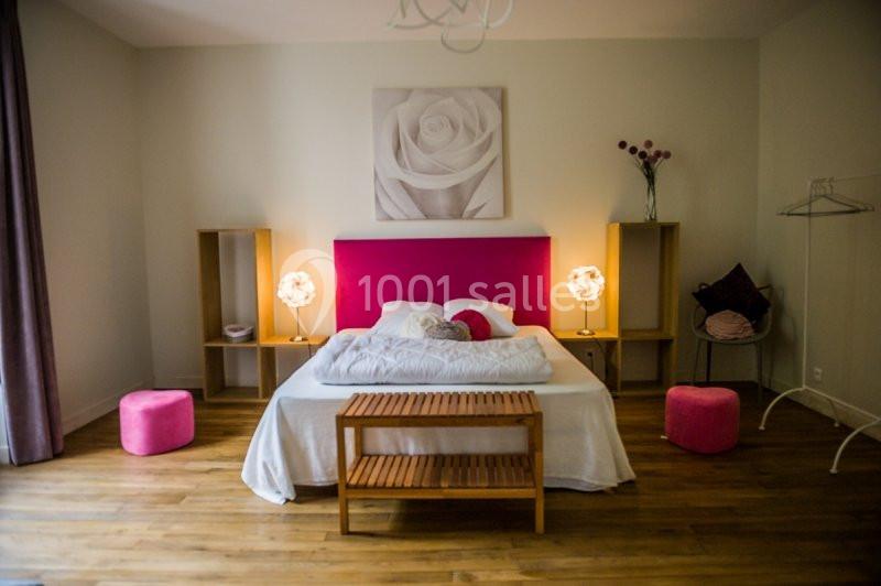 Chambre avec lit double, tête de lit rose, tables de chevet avec lampes, tabourets roses et parquet en bois.