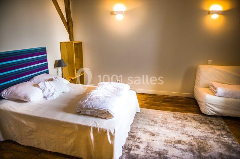 Chambre lumineuse avec lit double, tête de lit colorée, canapé blanc, parquet et éclairage mural.