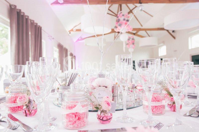 Salle de réception décorée avec des tons roses et blancs, tables dressées avec vaisselle, fleurs et bougies.