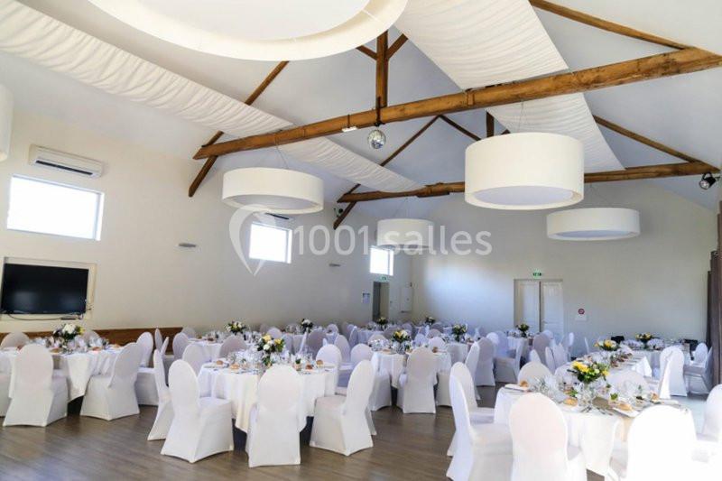 Salle de réception lumineuse avec tables rondes décorées de nappes blanches et bouquets de fleurs.