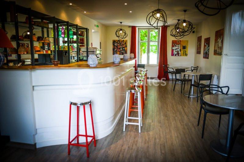 Intérieur d'un café lumineux avec un comptoir blanc, des tabourets colorés et des tables près de grandes fenêtres.
