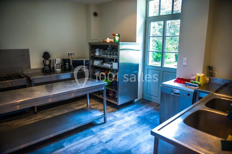 Cuisine équipée avec plans de travail en inox, étagères de rangement, électroménagers et lumière naturelle par une porte…