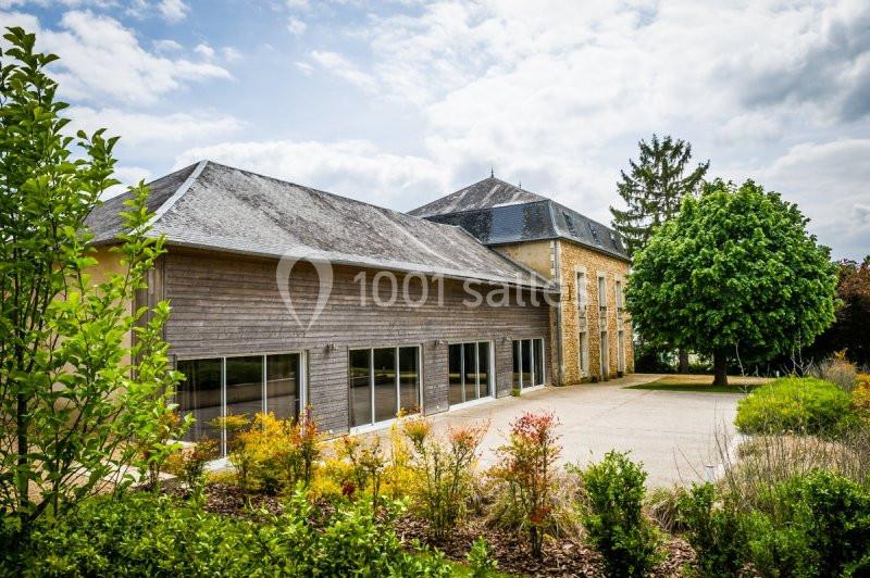 Bâtiment avec façade en bois et pierre, entouré de végétation, sous un ciel partiellement nuageux.