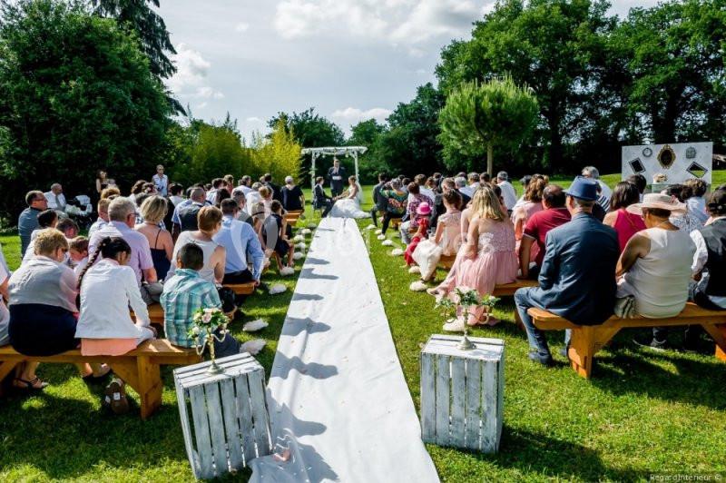 Cérémonie de mariage en plein air avec invités assis sur des bancs, allée centrale décorée et arche florale au fond.