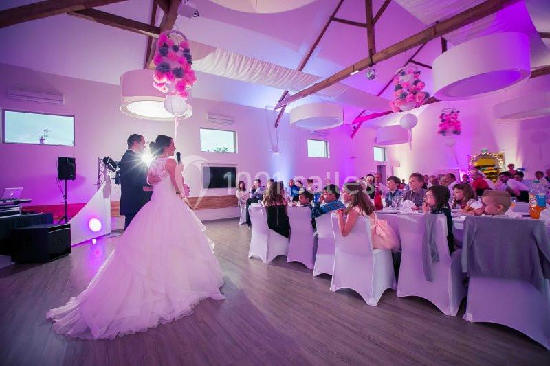 Un couple de mariés s'adresse à des invités assis dans une salle de réception décorée et éclairée en violet.
