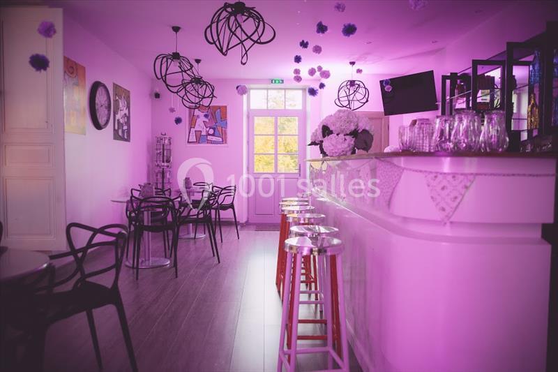 Salle de bar lumineuse avec décoration violette, comptoir blanc, tabourets hauts et chaises design noires.
