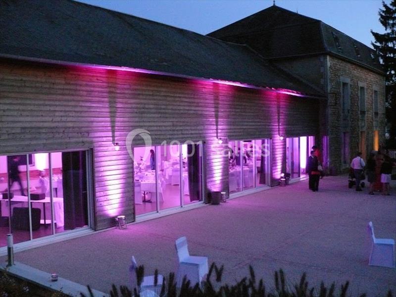 Façade d'un bâtiment en bois éclairée par des lumières roses, avec des baies vitrées donnant sur une salle aménagée.