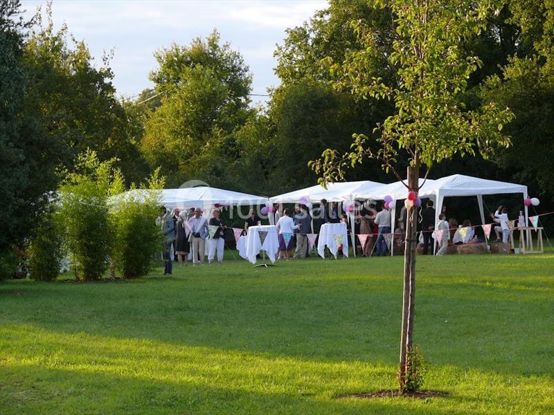 Groupe de personnes rassemblées sous des tentes blanches dans un parc verdoyant lors d'un événement en plein air.