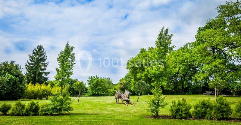 Un grand espace vert avec pelouse, arbres et une sculpture en bois sous un ciel partiellement nuageux.