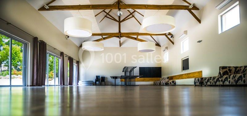 Salle spacieuse avec poutres apparentes, grandes fenêtres, mobilier minimaliste et lumière naturelle abondante.