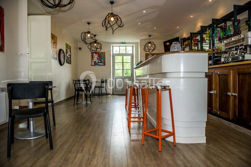 Intérieur d'un café avec un comptoir blanc, tabourets orange, tables, chaises et décorations murales colorées.