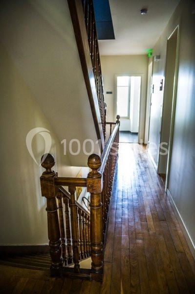 Escalier en bois avec rampe sculptée, situé dans un couloir lumineux avec parquet et murs clairs.