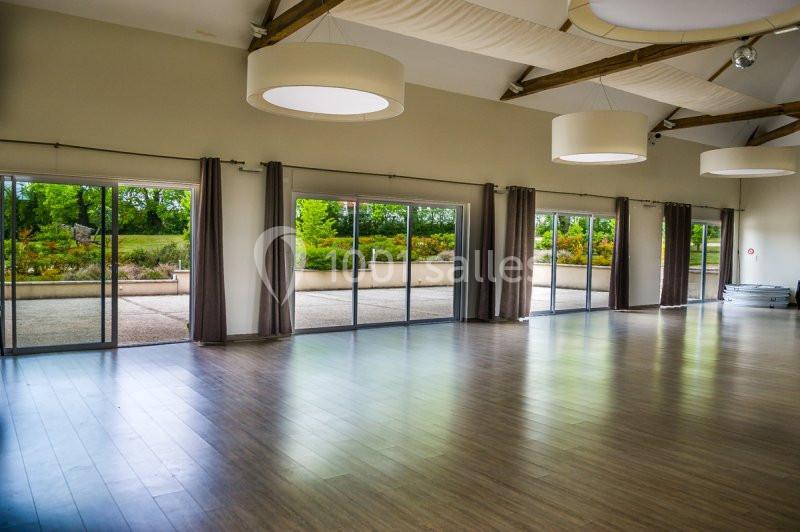 Salle lumineuse avec parquet, grandes baies vitrées donnant sur un espace extérieur verdoyant et ciel dégagé.