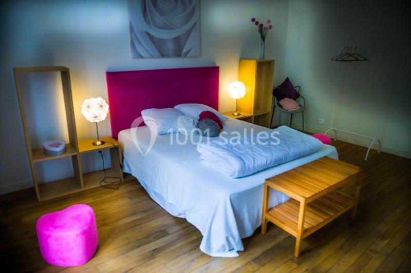 Chambre avec lit double, tête de lit rose, tables de chevet, lampes allumées et mobilier en bois sur parquet clair.