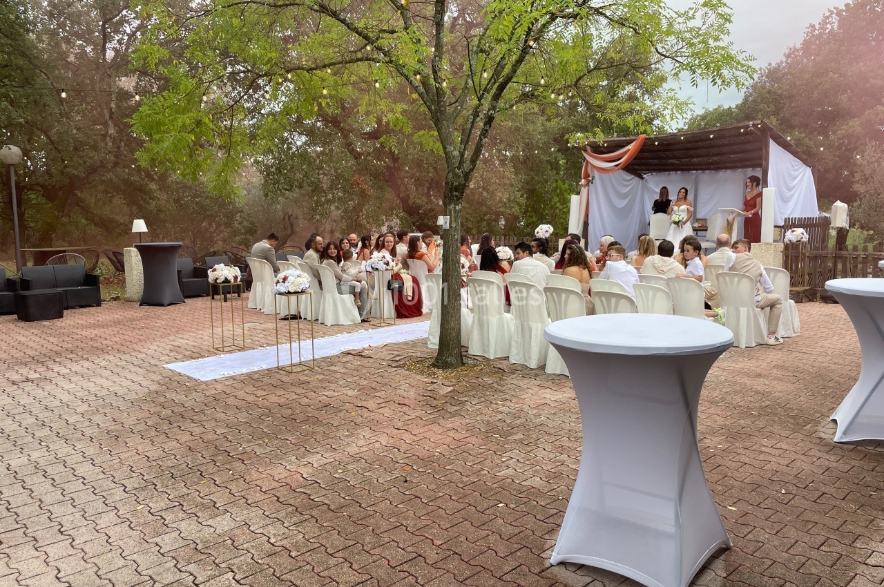 Cérémonie de mariage en plein air avec invités assis, décorations blanches et arche ornée de tissus.