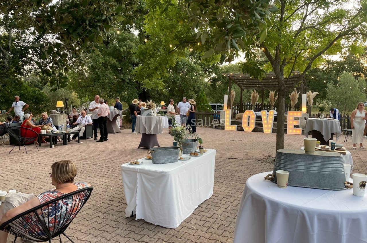 Personnes réunies dans un jardin pour une réception, avec des tables dressées et des lettres lumineuses formant ’LOVE’.