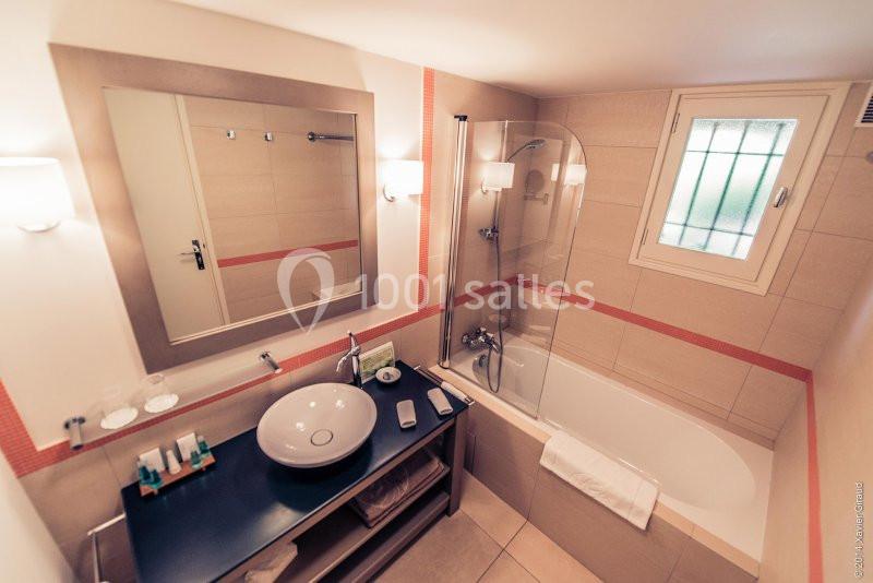 Salle de bain avec baignoire, lavabo moderne sur meuble noir, miroir mural et lumière naturelle par une fenêtre.