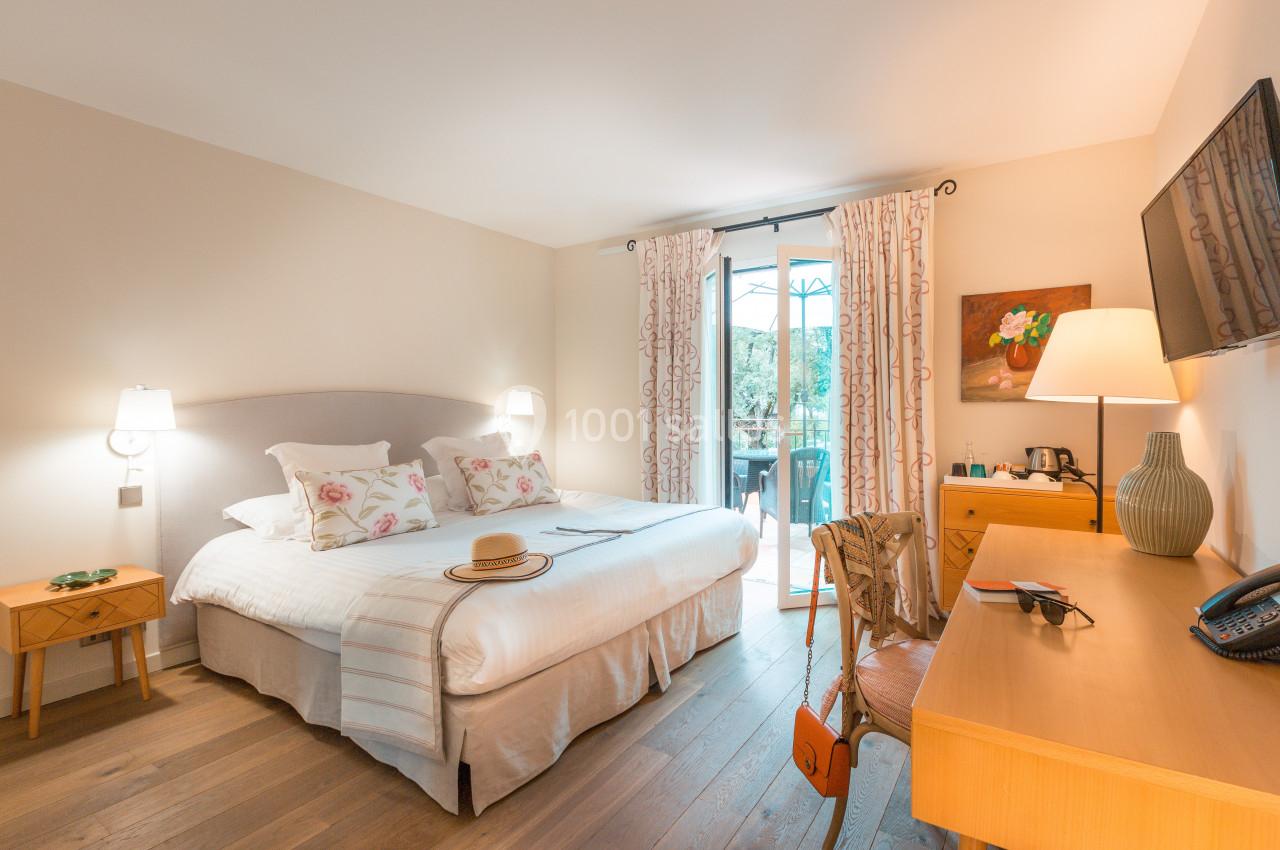 Chambre lumineuse avec lit double, bureau, télévision, et accès à un balcon donnant sur un espace extérieur verdoyant.