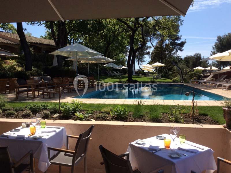 Terrasse d'un restaurant avec vue sur une piscine entourée de chaises longues, parasols et végétation.