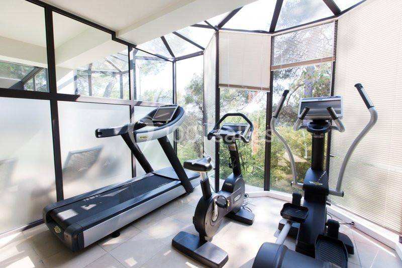 Salle de sport lumineuse avec tapis de course, vélo d'appartement et vélo elliptique près de grandes baies vitrées.