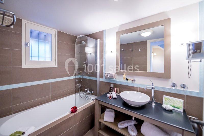Salle de bain moderne avec baignoire, lavabo sur meuble, miroir éclairé et fenêtre à barreaux.