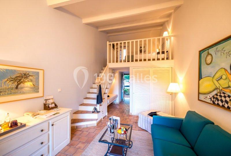 Salon lumineux avec canapé bleu, table basse, mezzanine en bois, escalier et décoration murale colorée.