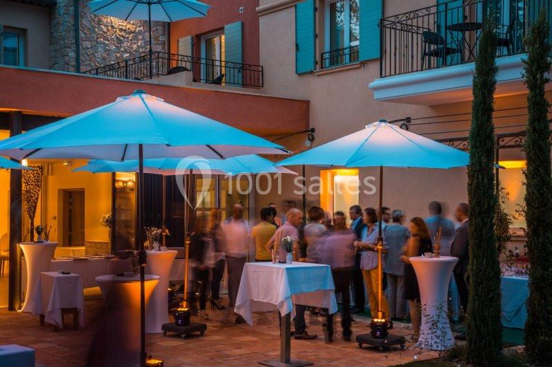 Groupe de personnes discutant sous des parasols éclairés dans une cour extérieure en soirée.