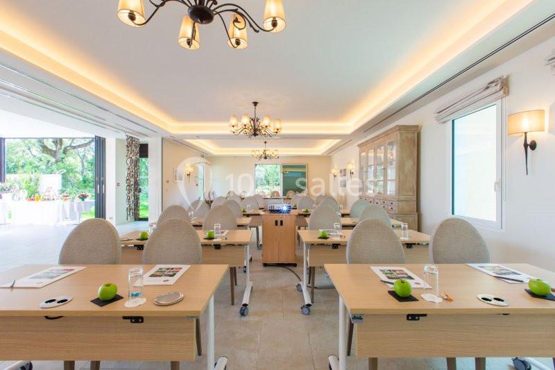 Salle de réunion lumineuse avec des tables équipées de documents, verres d'eau et pommes vertes, vue sur un jardin.