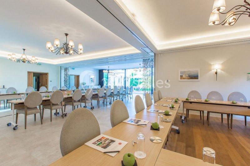 Salle de réunion lumineuse avec tables disposées en U, chaises rembourrées et vue sur un jardin à travers de grandes baies…