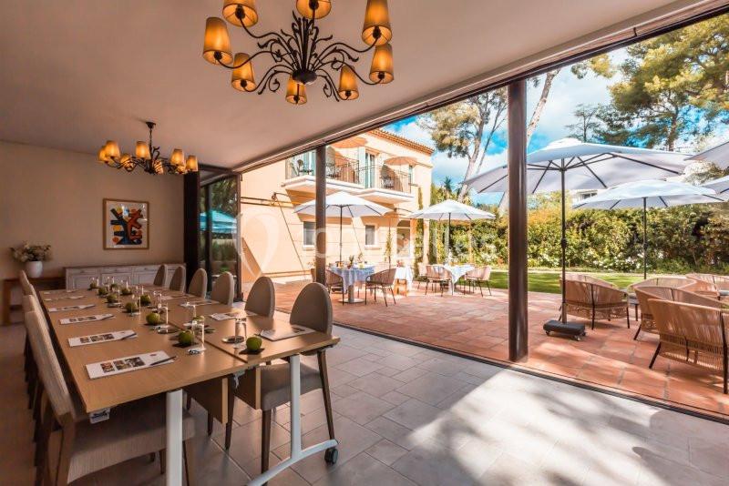 Salle de réunion lumineuse avec table dressée, ouverte sur une terrasse aménagée et un jardin verdoyant.
