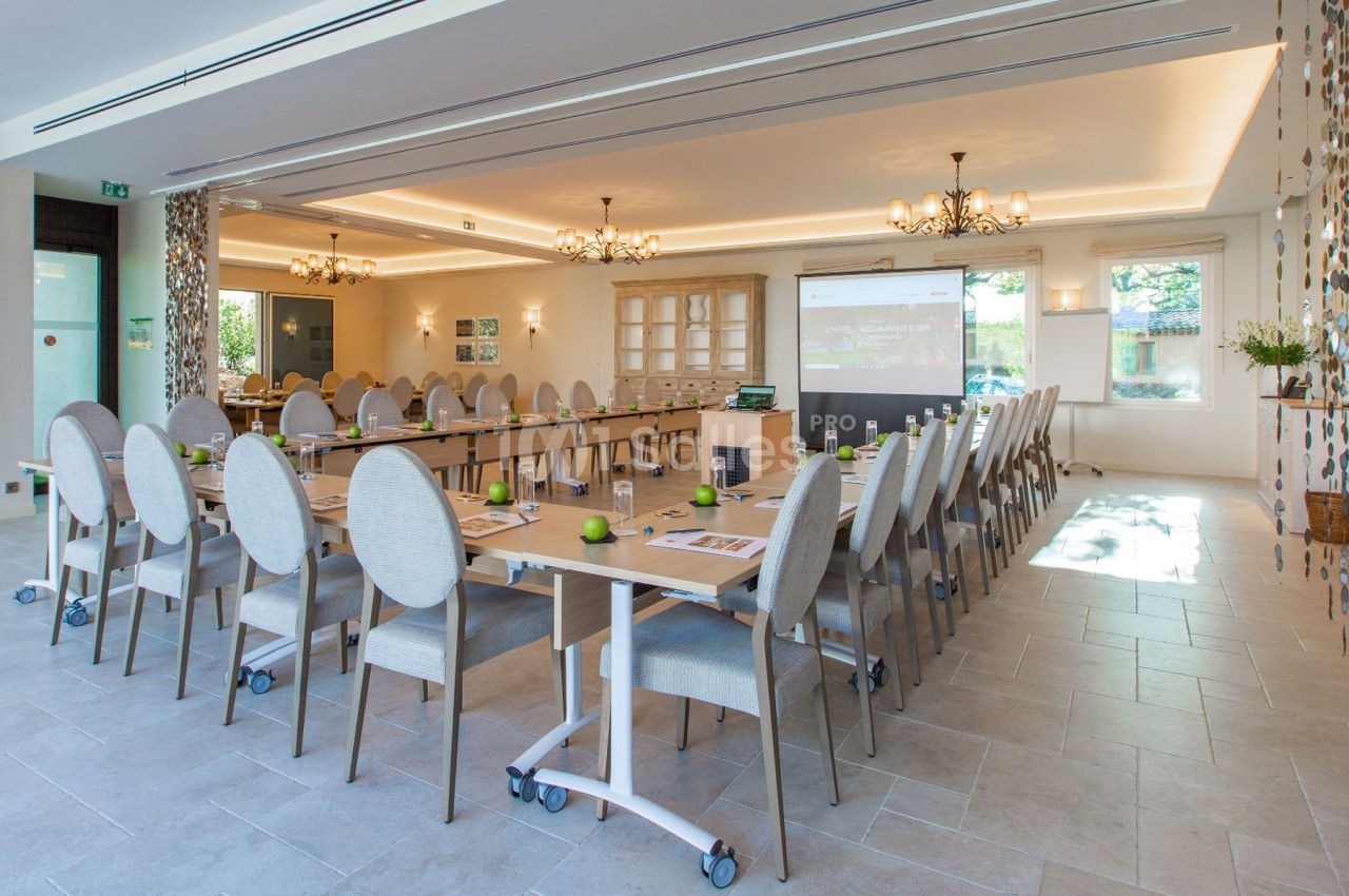 Salle de réunion lumineuse avec tables disposées en U, chaises rembourrées et écran de projection allumé.