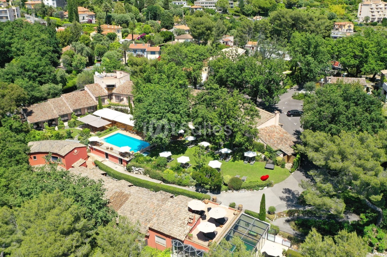 Vue aérienne d'un domaine avec piscine, jardins verdoyants, terrasses et bâtiments aux toits en tuiles entourés d'arbres.