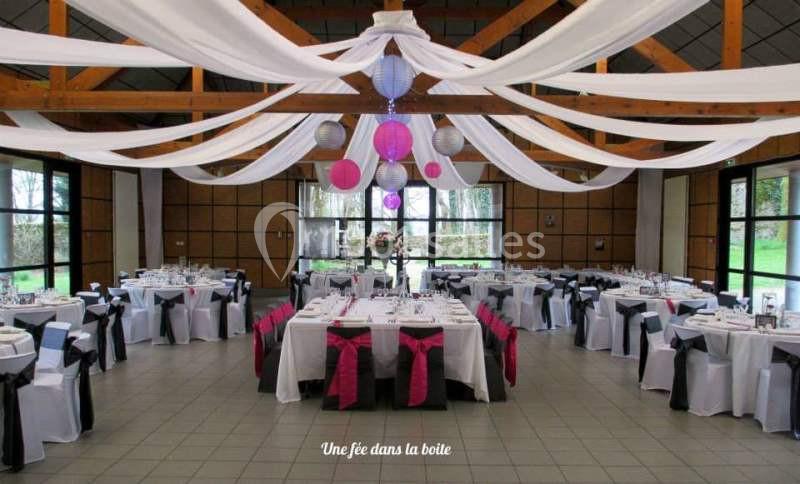 Salle de réception décorée avec des nappes blanches, des rubans colorés et des suspensions en papier au plafond.