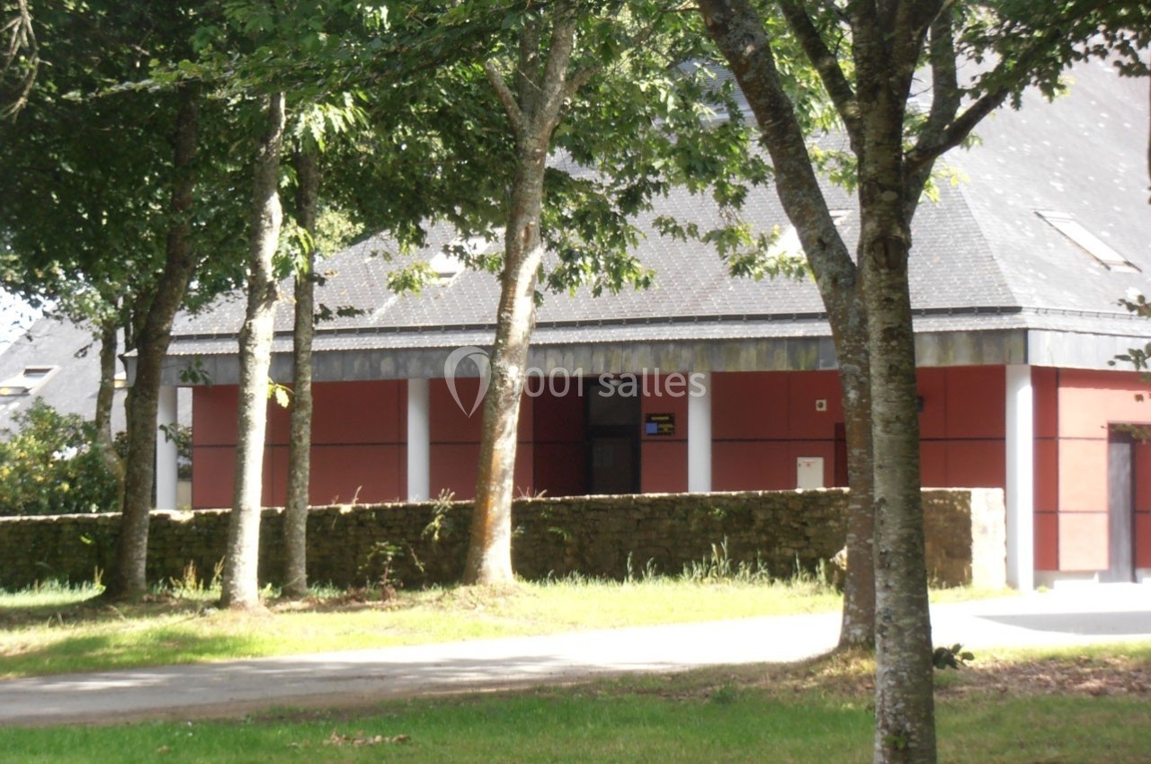 Bâtiment en pierre et crépi rouge entouré d'arbres, avec un chemin et une pelouse au premier plan.