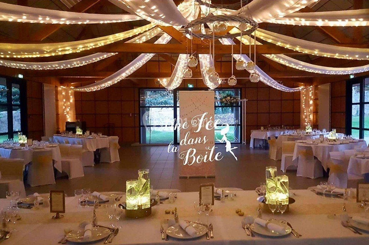 Salle de réception décorée avec des guirlandes lumineuses, des tables dressées et un panneau lumineux au centre.