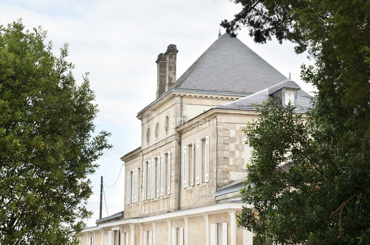 Façade d'un bâtiment en pierre à deux étages, entouré d'arbres et bordé d'une allée gravillonnée.