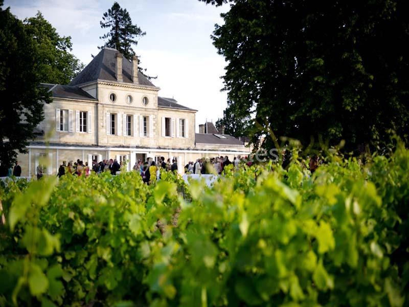 Façade d'un bâtiment élégant entouré de vignes et d'arbres, avec des personnes rassemblées à l'extérieur.