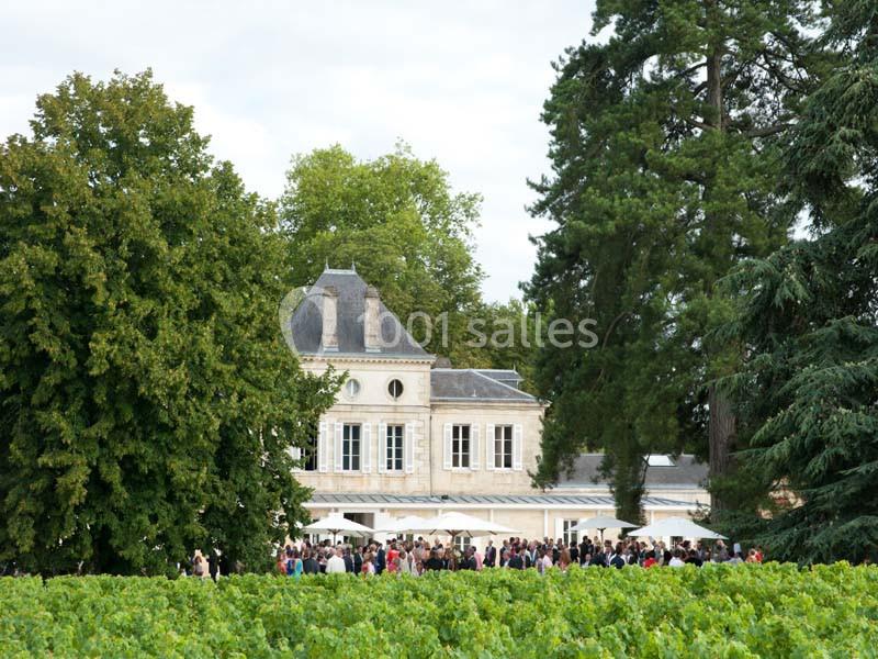 Un château entouré de vignes et d'arbres, avec une foule rassemblée près de terrasses ombragées.