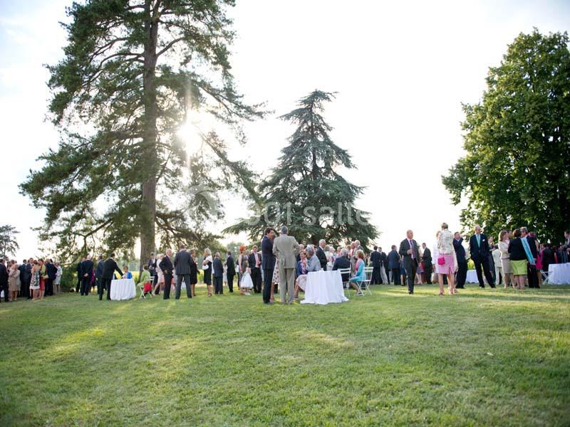 Groupe de personnes rassemblées dans un parc lors d'un événement en plein air, avec des tables et des arbres en arrière-plan.