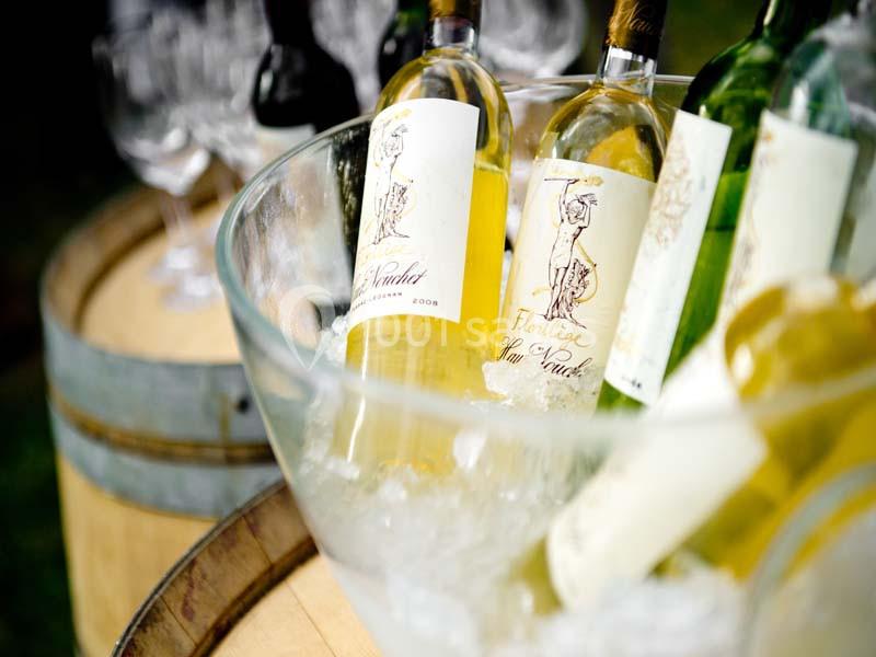 Bouteilles de vin blanc refroidies dans un seau en verre rempli de glace, posées sur un tonneau en bois.