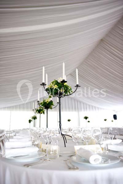 Salle de réception décorée avec des tables rondes, nappes blanches et chandeliers ornés de fleurs.