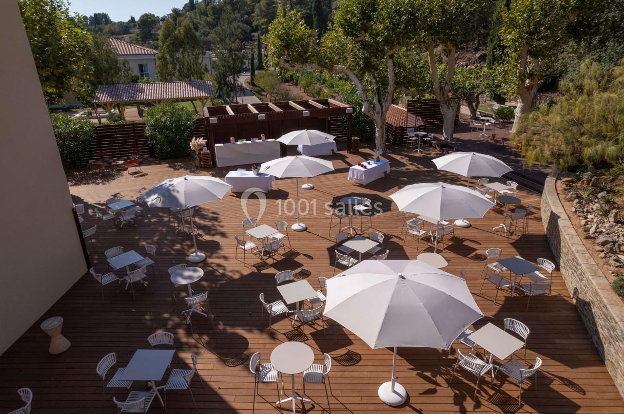 Terrasse en bois aménagée avec des tables, des chaises et des parasols blancs, entourée de végétation.