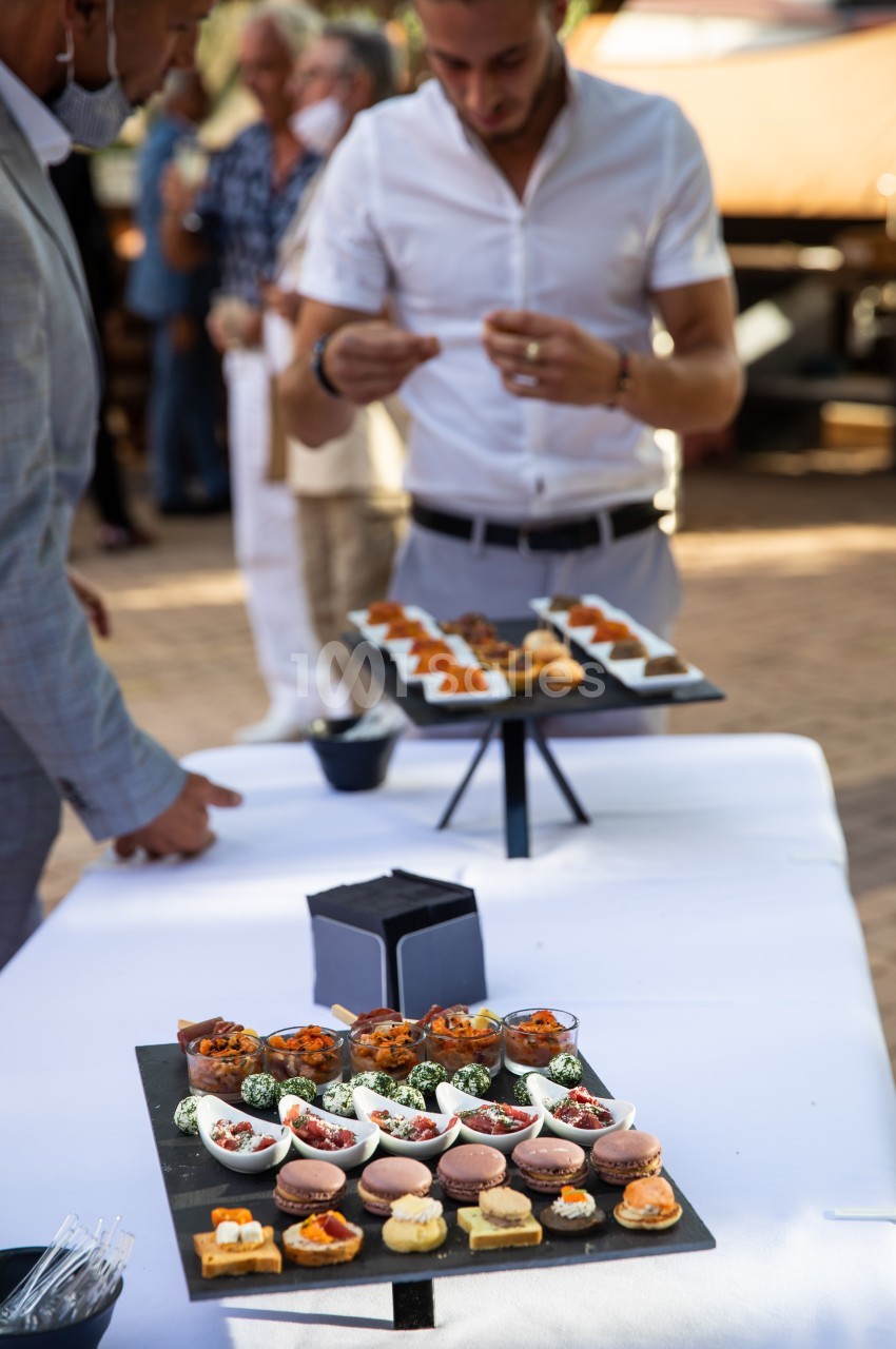 Plateaux de bouchées apéritives variées disposés sur une table lors d'un événement en extérieur.