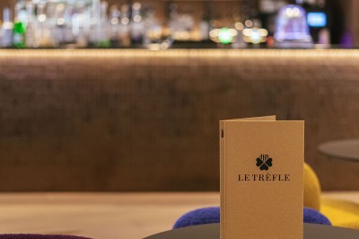 Miniature Bar Menu posé sur une table ronde dans un bar élégant avec un comptoir éclairé en arrière-plan.