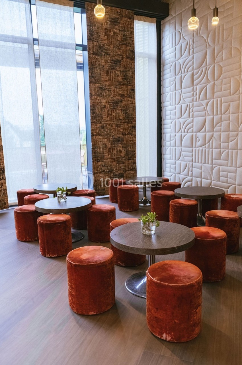 Salle moderne avec tables rondes, poufs en velours rouge et murs décorés de motifs géométriques en relief.