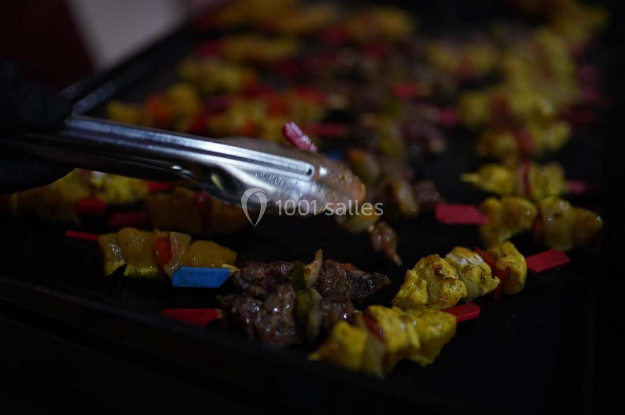 Location salle Crosne (Essonne) - Aux Tulipes #7 Brochettes de viande et légumes colorés grillées sur une plaque chauffante, manipulées avec une pince en métal.